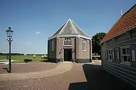 Photographie en couleurs d'un bâtiment précédé par une maison au premier-plan