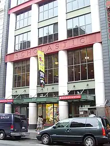 Façade vitrée d'un immeuble comportant quatre colonnes blanches. Au 2/3 de hauteur de la photo est visible le nom de l'éditeur « Scholastic » sur fond rouge.