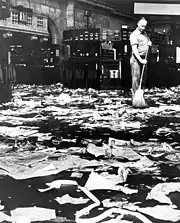 Photo noir et blanc d'un employé balayant une pièce jonchée de papiers abandonnés