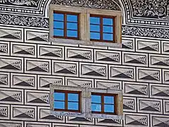 Vue des sgraffites en forme de bossages d'une façade, percée de quatre petites fenêtre à carreaux.