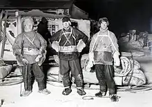 Photographie noir et blanc de trois hommes en tenue pour pour la marche (raquette, manteau, bonnet).