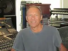 un homme avec un tshirt gris se tenant devant une console de studio.