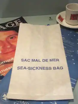 Sac à vomi de couleur blanche avec l'inscription en bleu « Sac mal de mer » et sa traduction en anglais.