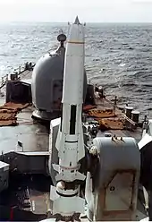 Un grand missile blanc placé sur son lanceur à l'avant d'un navire de guerre.