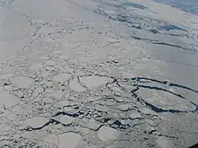 Cette image est une photographie aérienne sur laquelle on peut voir une parie de la côte du Labrador et de l'océan Atlantique en hiver. De nombreuses masses de glace plus ou moins proches les unes des autres recouvrent presque entièrement la surface de l'eau, rendant la navigation difficile.