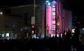 La nuit, Sean Penn Parle dans un haut-parleur à une foule de manifestants devant un bâtiment portant l'enseigne « Castro », une perche prend le son au-dessus d'eux