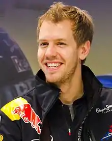 Sebastian Vettel, en costume Red Bull, sourit aux caméras.