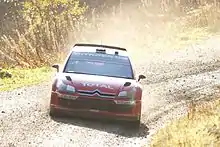 Citroën C4 WRC de Sébastien Loeb, livrée rouge, vue de face en sortie de virage sur un sol boueux.