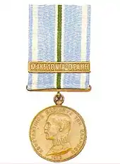 Photographie d'une médaille dorée montrant le profil d'un homme, avec un ruban blanc, bleu et vert.