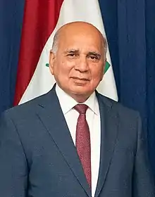 Photo-portrait d'un homme en costume et cravate sur fond d'un drapeau irakien.