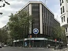 Photographie d'un bâtiment prise depuis la rue. Sur la façade vitrée, un logo rond avec les lettres en majuscule P et P sur fond bleu.