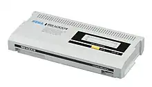 Photographie d'une console rectangulaire blanche, avec une partie noire sur le côté supérieur droit, et où est inscrit Sega en bleu à gauche.