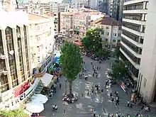 Une rue relativement occupée de personnes à pied et de panneaux de magasins, vue de quelques étages de hauteur.