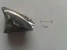 Photographie rapprochée d'un cristal de sélénium sur fond blanc, à proximité d'une échelle pour mesure.