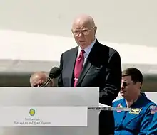 Un Glenn à lunettes s'exprimant sur un podium en plein air