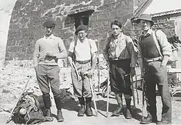Photographie en noir et blanc de quatre hommes devant un refuge de montagne.