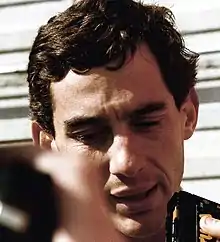 Photo d'Ayrton Senna en portrait serré sur son visage ; les micros des journalistes apparaissent sur les bords de l'image.