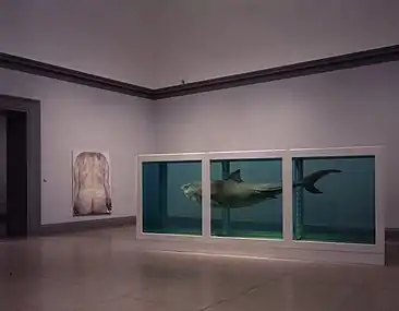 salle d'exposition contenant un tableau représentant un dos nu et un parallélépipède bleuté contenant un requin mort