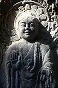 Photographie d'une sculpture en pierre d'un bouddha souriant.