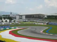 Piste goudronnée de Formule 1 au niveau d'une chicane, avec une tribune en arrière-plan.