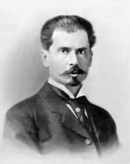 Photographie ancienne en noir et blanc, de trois quarts, du visage d’un homme portant une moustache et une barbe courte.