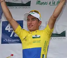 Photographie d'un homme en plan américain, vu de trois-quarts, avec un maillot jaune et bleu, les bras levés.