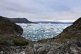 Photographie en couleurs de roches affleurantes baignées les eaux d'un fjord