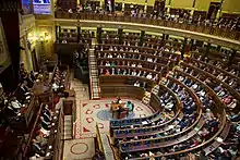 Photographie d'une salle de réunion parlementaire en forme d'hémicycle au cours d'une séance.