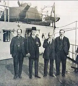 Quatre hommes en costume sur le pont d'un bateau.