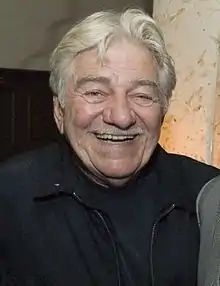  Photographie en buste d'un homme aux cheveux gris portant une veste noire.