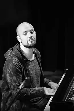 photo noir et blanc d'un homme, barbu et chauve, assis au piano