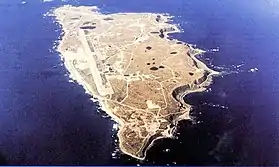 Photo aérienne en couleur de l’île Shemya, avec Eareckson Air Station visible sur le coin sud-est de l’île.