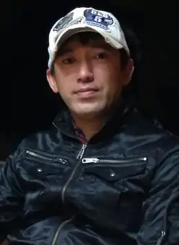 Photo en couleur d'un homme asiatique portant un blouson noir et une casquette blanche.