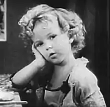 photo en noir et blanc d'une petite fille blonde la tête appuyée sur la main