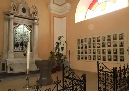 photo de chapelle avec fonts baptismaux au centre, autel à gauche, et une série de photos sur le mur de droite.