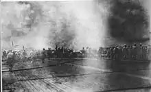 Photo en noir et blanc d'un pont d'envol sur lequel des hommes sont regroupés devant une épaisse fumée noire