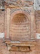Vue d'une niche dans un mur, décorée de motifs géométriques et brique rouge et pierre blanche.