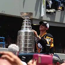 Photographie de Crosby avec un maillot noir lors de la parade des Penguins et tenant la Coupe Stanley dans les mains