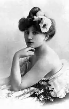Photo ancienne d’une jeune fille, bras et épaules nus, des fleurs dans ses cheveux relevés en épais chignon, de trois quarts