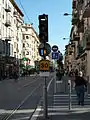 Image représentant un feu tricolore de tramway avec la barre horizontale marquant l’arrêt, le SAC avec losange orange indiquant la prise en charge de la priorité et le point d’exclamation bleu indiquant le passage à la barre verticale allumés, ainsi que la vitesse limitée à 30 km/h à la station Palais des expositions.