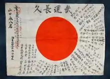 Petite pièce de tissu sur laquelle il y a un drapeau japonais entouré de phrases porte-bonheur.