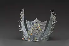 Photoraphie d'une couronne de forme allongée en métal, posée sur une suface neutre.