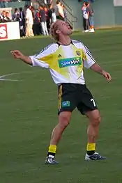 photo d'un footballeur en short noir et maillot blanc et jaune levant la tête en attendant un ballon