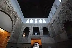 La photo panoramique, prise en contre-plongée, montre trois des quatre murs de la salle de la synagogue, avec au centre le mur sud, ainsi que son plafond fait d'une voûte de bois sombre. Les murs, d'une couleur blanc cassé, sont ornés de bas-reliefs et d'arches de style mudéjar et d'inscriptions en hébreu.