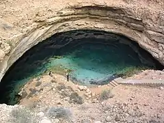 Doline dans un sol rocheux, avec une étendue d'eau en son fond.