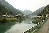 Photo couleur d'un pont suspendu au-dessus d'une rivière sur fond de paysage de montagne.