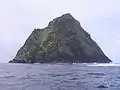 Photographie couleur d'une île de forme triangulaire, aux falaises sombres, s'élevant au-dessus de la mer.