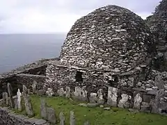 Photographie en couleurs d'un bâtiment en forme de dôme et appareillé de pierres grises et blanches, un cimetière venant le longer au premier plan.