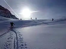 Skieurs de randonnée ayant fait une trace en Z dans de la poudreuse, sous un soleil éblouissant.