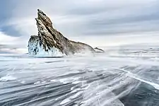 La mer gelée est constellée de zébrures glacées. Un rocher pointu se dresse vers le ciel grisatre.